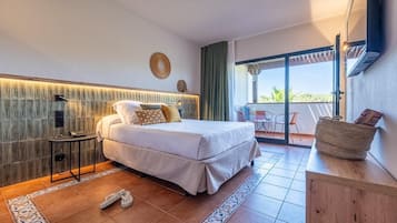 A modern hotel room with a large bed, a small table, a chair, and a balcony with a view.