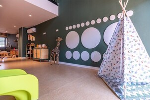 Zona de juegos infantiles con una estatua de jirafa, un tipi y una pared con diseños circulares.