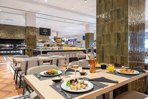 Un restaurante con zona de bufé, mesas de comedor con platos de comida y una botella de vino Cesta Moscana.