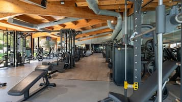Un gimnasio con diferentes equipos de ejercicio, vigas de techo de madera y vistas despejadas al exterior.
