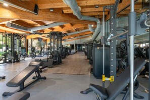 Een sportschool met diverse fitnessapparaten, houten balkenplafond en vrij uitzicht op het omliggende landschap.
