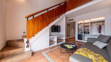 Una sala de estar moderna con una escalera, un sofá, una mesa de centro y un televisor.