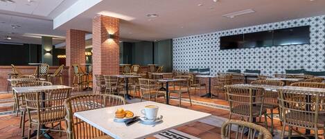 Un'ampia sala da pranzo interna con diversi tavoli e sedie in vimini, caratterizzata da un muro decorato e una TV a schermo piatto montata sulla parete.