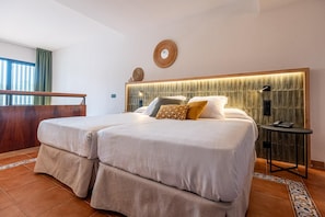 Un lit double avec une tête de lit en bois, deux tables de chevet et une vue sur l’extérieur par une fenêtre avec des rideaux.