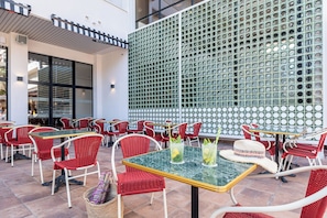 An outdoor seating area with red wicker chairs and tables, a green perforated wall, and a tiled floor. - Estival Park Marena (Vila-Seca)
