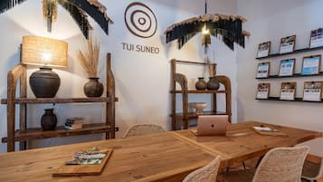 Un salón de conferencias con una mesa de madera, sillas de mimbre, un ordenador portátil y jarrones decorativos.