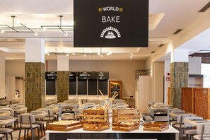 A modern cafe with a central counter displaying bread and pastries, surrounded by seating. - Estival Park Marena (Vila-Seca)