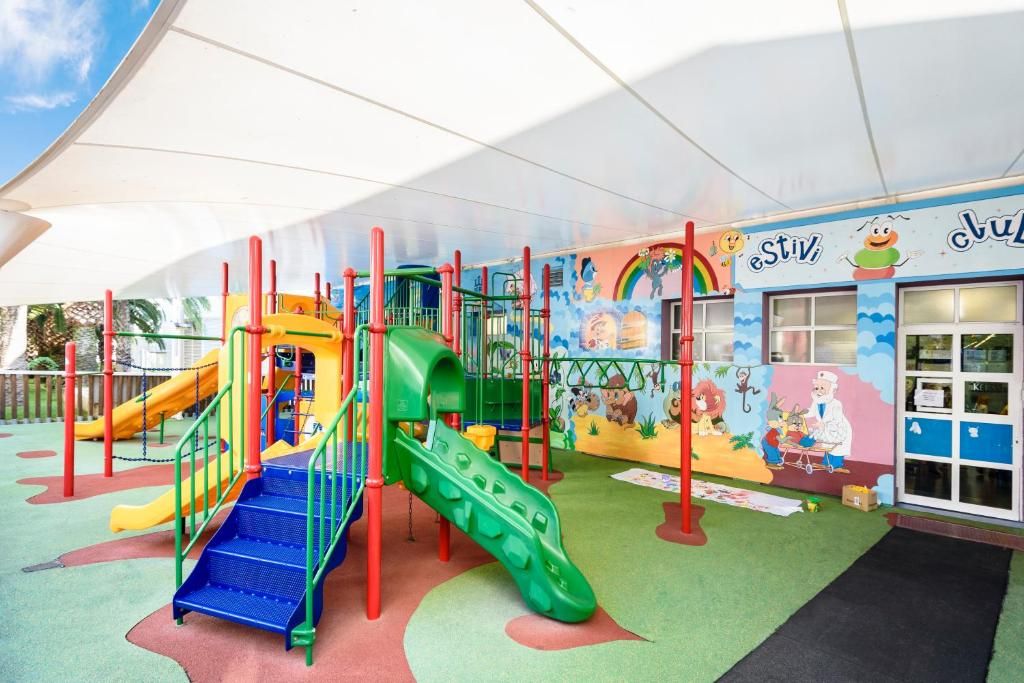 A children's play area with colorful slides and climbing structures, a mural with cartoon characters, and a building entrance with a sign.