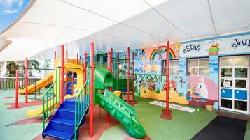 A children's play area with colorful slides and climbing structures, a mural with cartoon characters, and a building entrance with a sign.