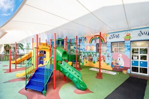 A children's play area with colorful slides and climbing structures, a mural with cartoon characters, and a building entrance with a sign. - Estival Park Marena (Vila-Seca)