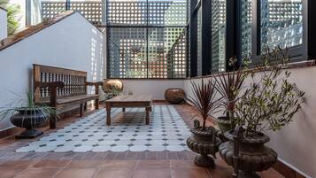 A sunlit patio with a wooden bench, a small table, and potted plants.