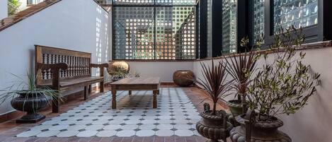 A sunlit patio with a wooden bench, a small table, and potted plants.