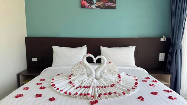 Quarto de hotel com cama decorada com toalha em formato de cisne e pétalas de rosa.