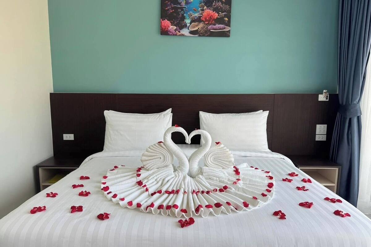 A hotel room with a bed featuring a swan towel design and rose petals.