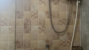 Área de chuveiro com chuveiro manual e painel de controle fixado na parede.