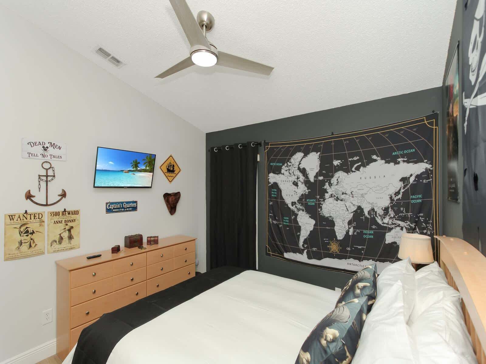 A bedroom with a bed, a dresser, a ceiling fan, a TV, and a world map on the wall.