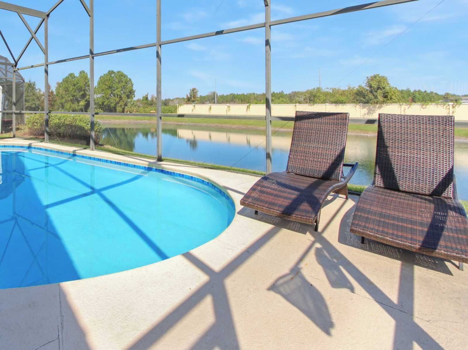 Piscina techada al aire libre con dos sillones de mimbre y vistas a un cuerpo de agua y vegetación.