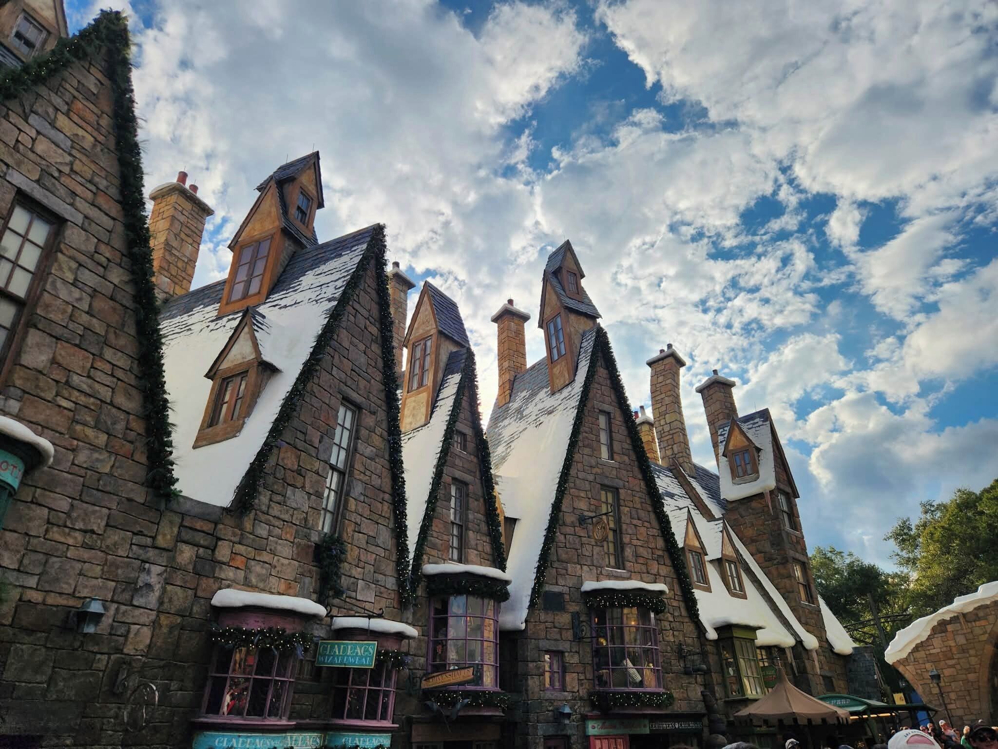 A row of traditional stone buildings with steeply pitched roofs, some with snow on the eaves, and a clear sky with clouds.