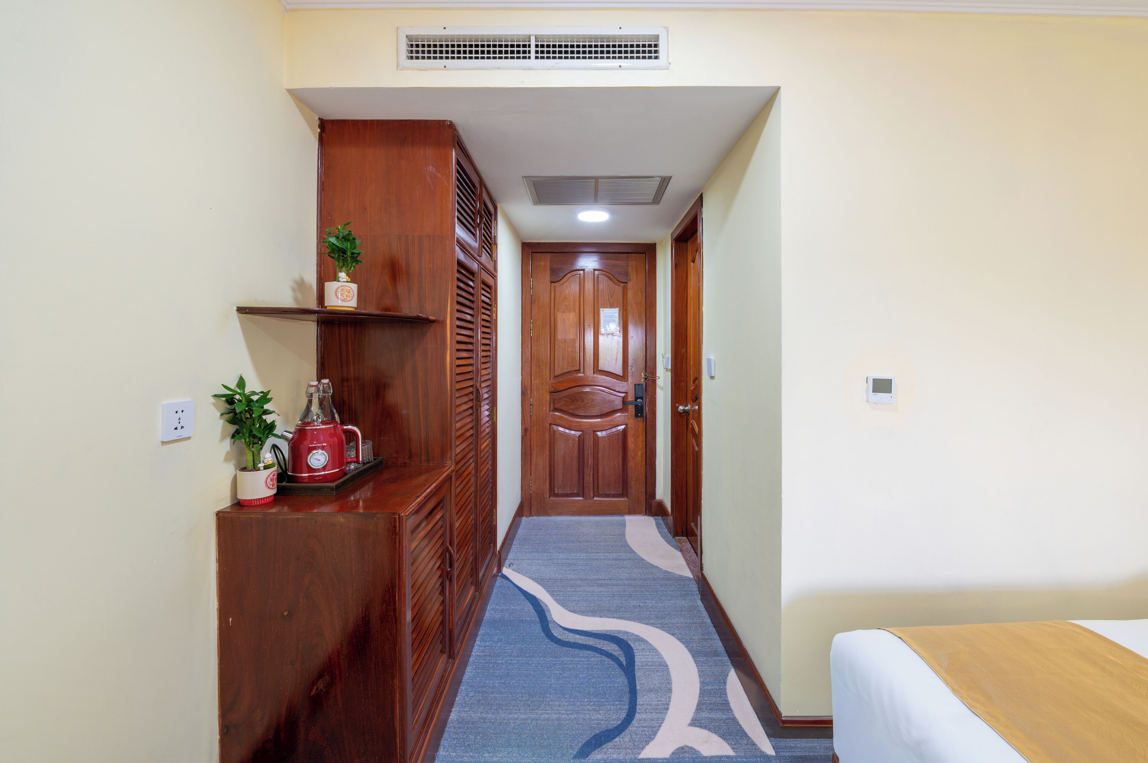 A hotel hallway with a wooden reception desk, a red kettle, and a blue patterned carpet.