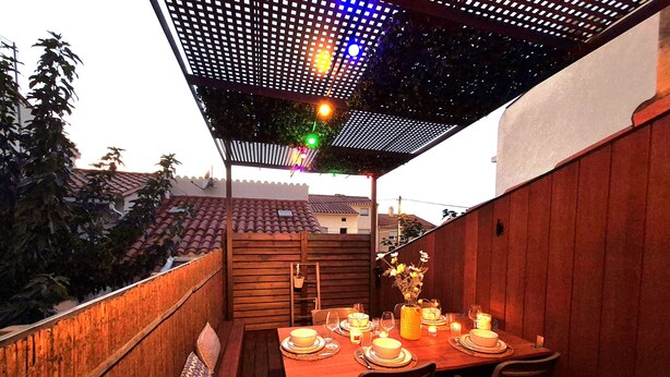 Une terrasse en bois avec une table dressée pour le repas, entourée de rampes en bois et agrémentée d’une pergola à motifs ajourés.