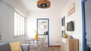 Un espace de vie compact comprenant un canapé, une table à manger avec des chaises, un coin cuisine et un téléviseur fixé au mur.