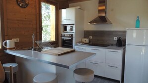 A modern kitchen with a central island, white cabinetry, a stainless steel range hood, and a refrigerator.