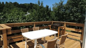 A wooden deck with a white table and wicker chairs, surrounded by a wooden railing.