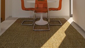 Ett modernt matområde med ett vitt bord och orange stolar, en färgstark, abstrakt målning på väggen och en mönstrad matta på golvet.