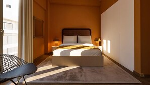 Ett modernt hotellrum med en stor säng, sänglampor, ett litet bord och utsikt över staden.
