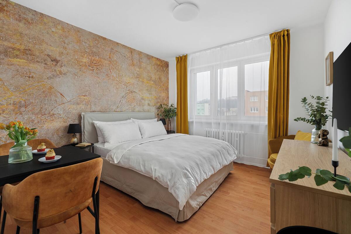 Ein modernes Hotelzimmer mit einem großen Bett, einem Schreibtisch und Blick auf die Stadt durch transparente Vorhänge.