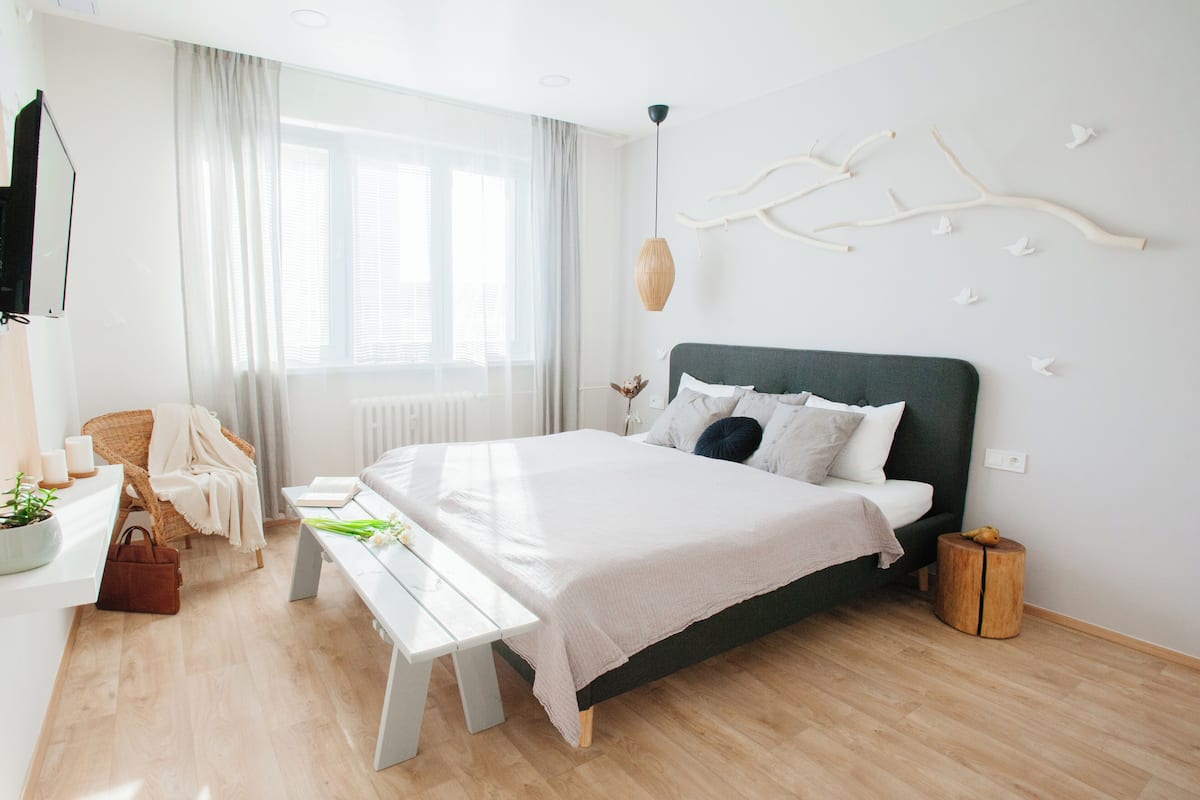 Ein modernes Schlafzimmer mit einem großen Bett, einem Nachttisch, einer Bank, einem Stuhl und einem Fenster mit Vorhängen.