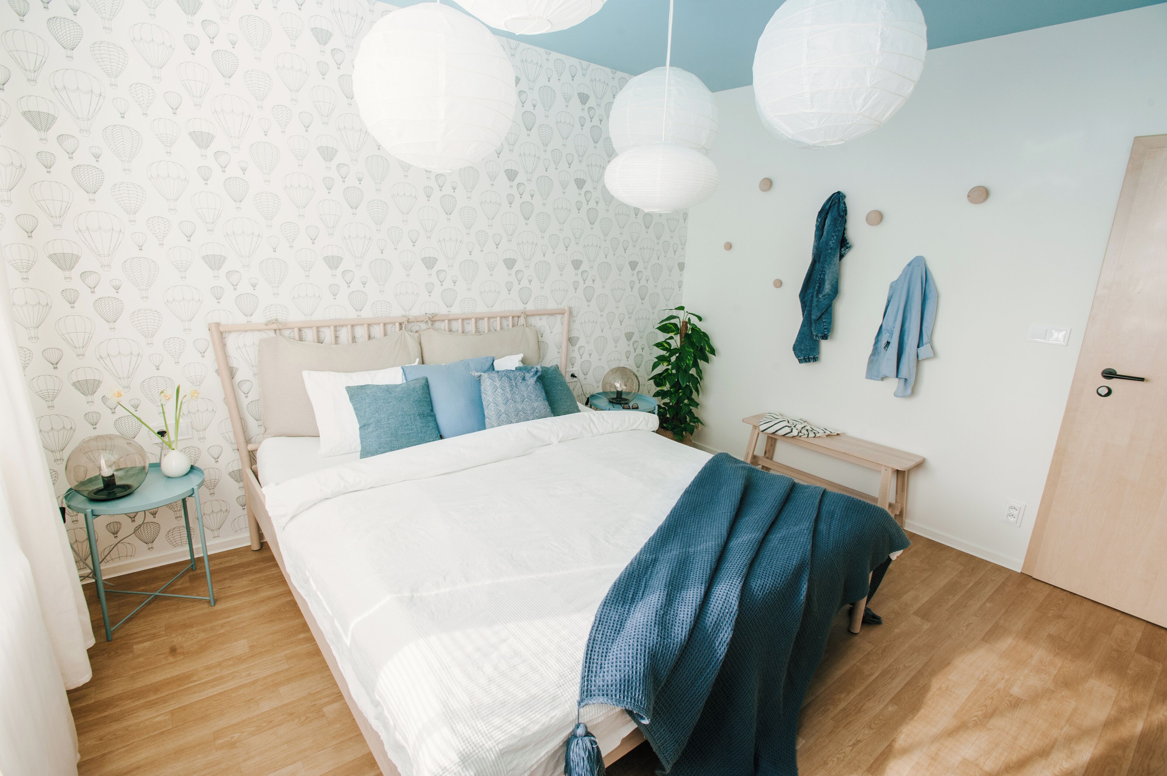 A bedroom with a bed, bedside table, hanging lights, and a wall with a pattern.