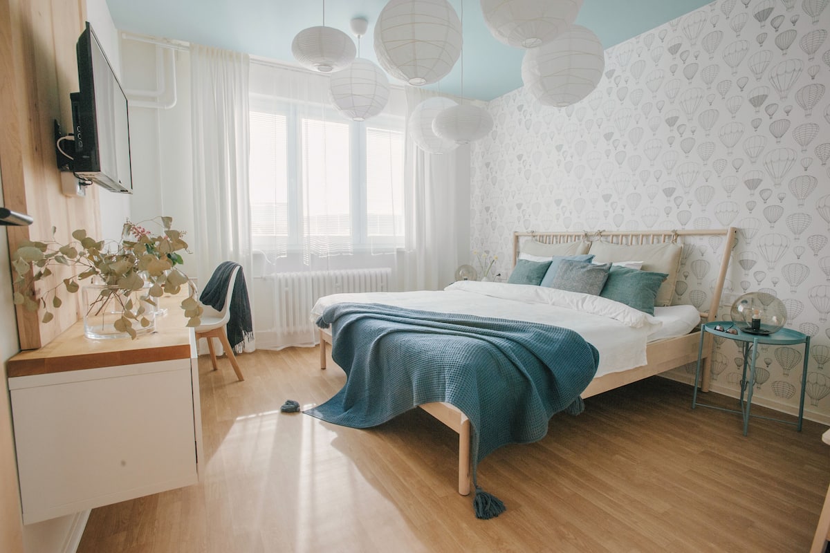 Ein Schlafzimmer mit einem hölzernen Bett, weißer Bettwäsche, einem Nachttisch mit Lampe und einem Fenster mit Vorhängen.