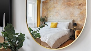 Une chambre à coucher moderne avec un grand lit, une table de chevet, une lampe et un miroir qui reflète la pièce.