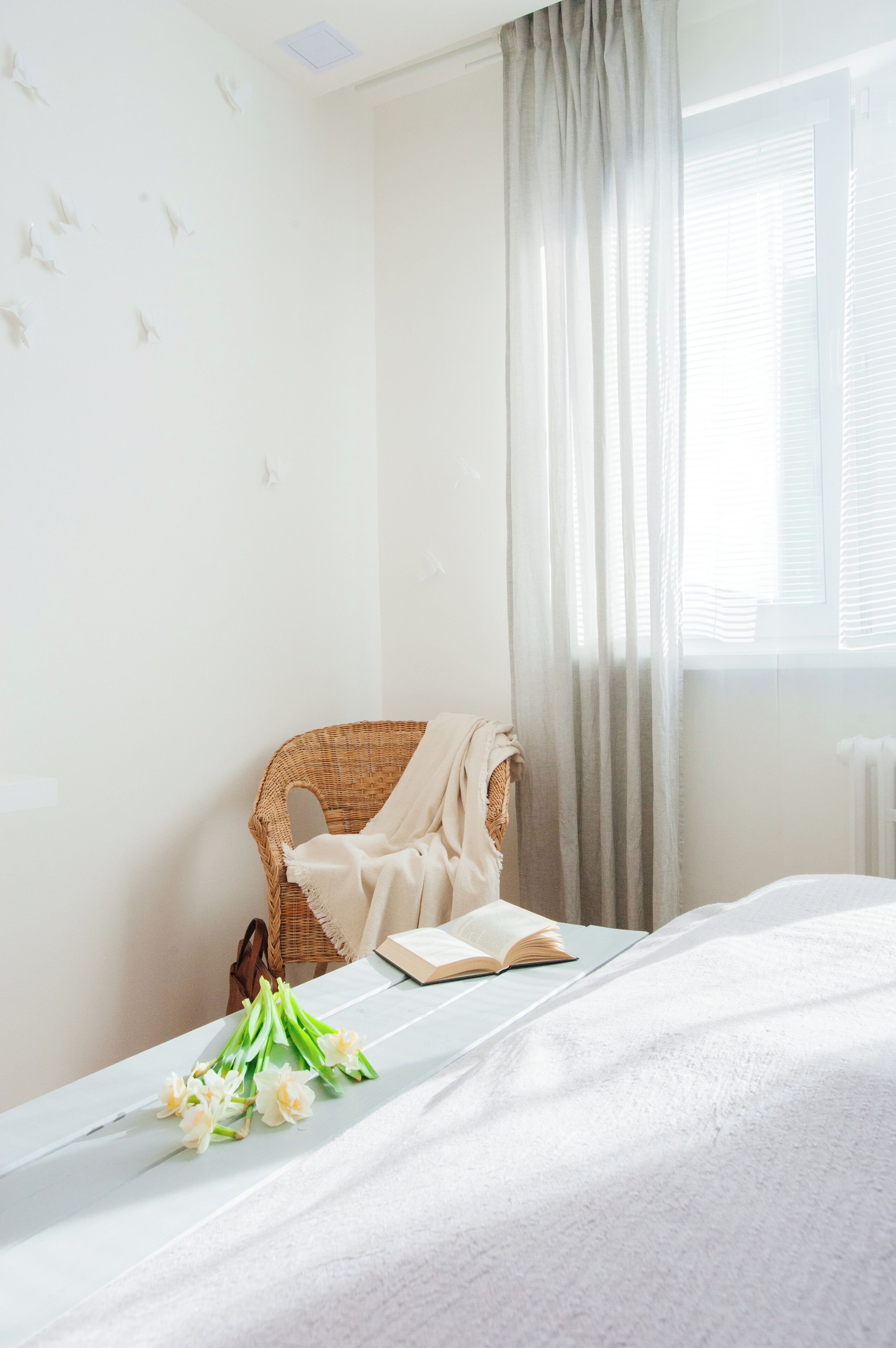 Une chambre à coucher bien rangée, avec un lit, une chaise en osier, un livre et un bouquet de fleurs posé sur le lit.