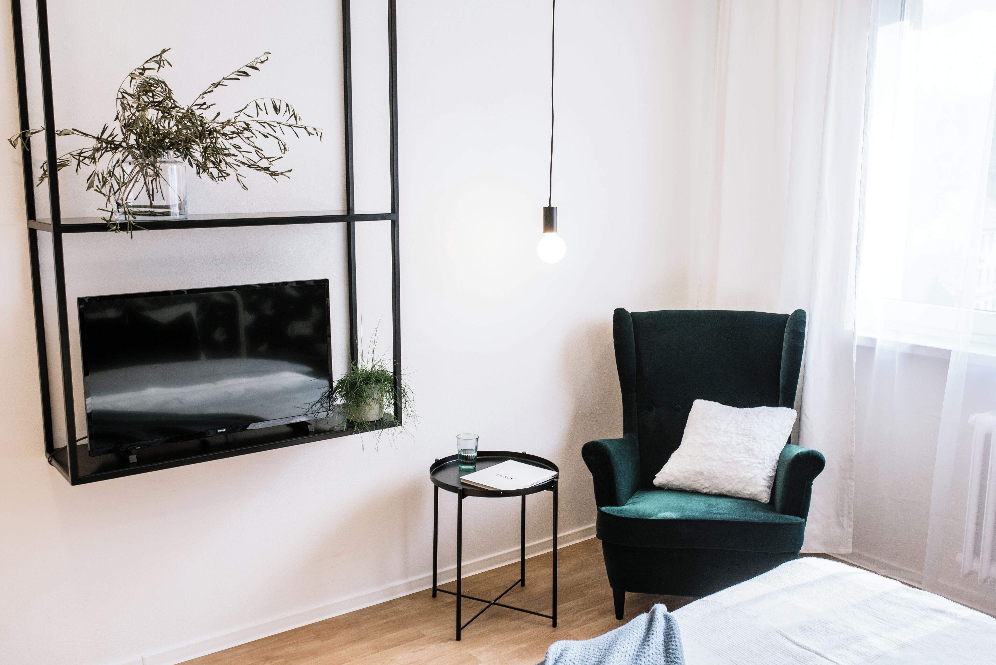 A modern room with a black-framed TV, a green armchair, a small side table, and a hanging light bulb.