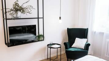 A modern room with a black-framed TV, a green armchair, a small side table, and a hanging light bulb.