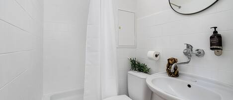 A bathroom with white tiles, a bathtub, a toilet, a sink, a mirror, and a small plant.