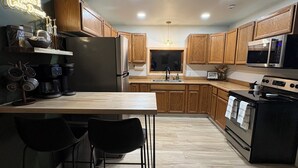 A modern kitchen with wooden cabinets, a stainless steel refrigerator, a microwave, and a stove. There is a wooden countertop with a sink and a window above it. - Barrel Sauna + Open Concept + Mountain Getaway = Relaxing Stay (Wasilla)