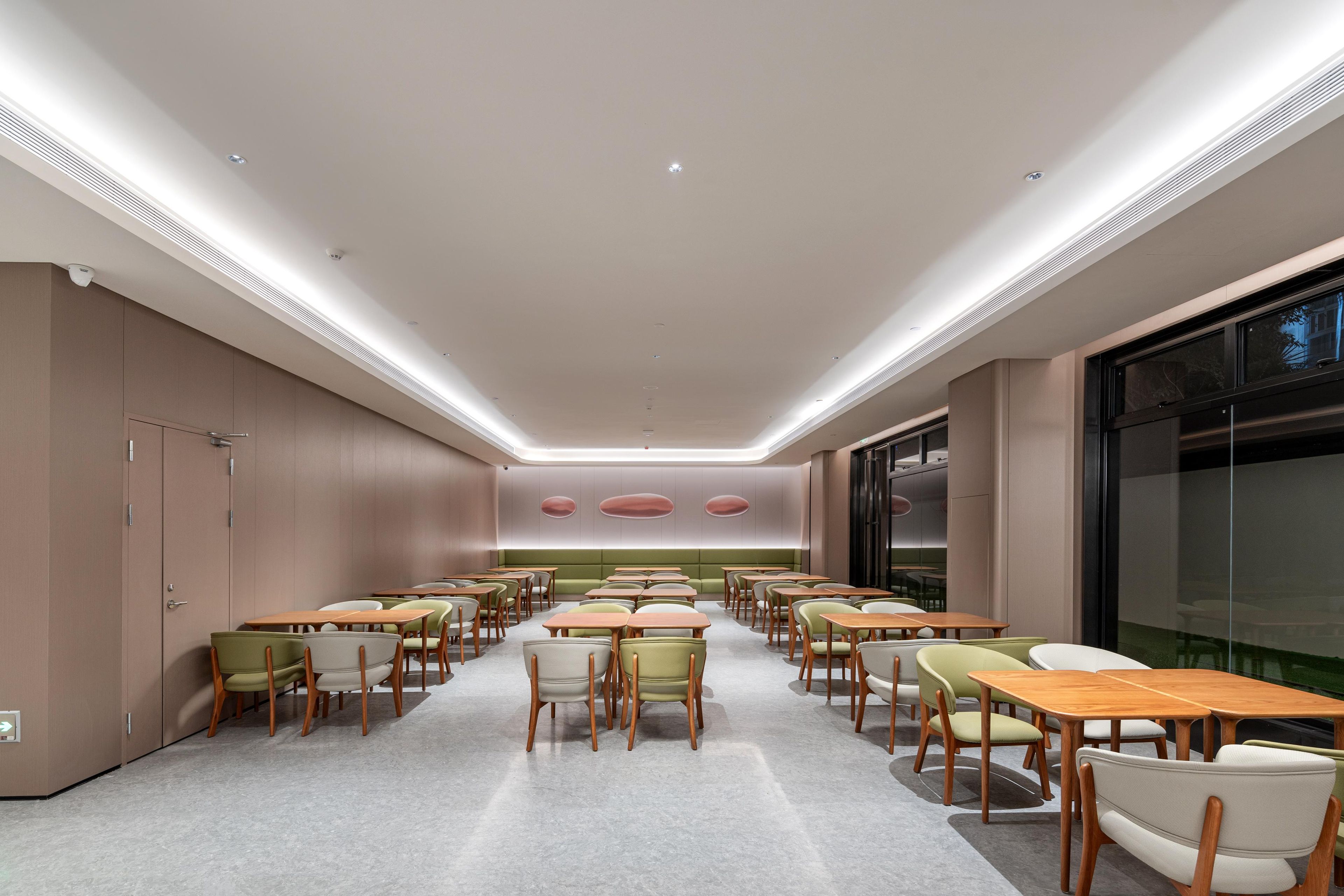 Een moderne vergaderzaal met meerdere tafels en stoelen, inbouwverlichting en een groot raam.