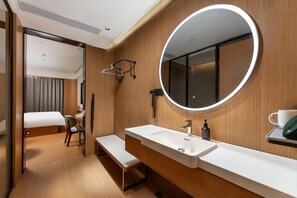 A modern hotel room with a large round mirror, a white sink, a bench, and a bed with a curtain. - Ji Hotel (Guangzhou)