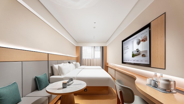 A hotel room with a bed, a seating area with a table, a TV mounted on the wall, and a window with curtains. - Ji Hotel (Guangzhou)