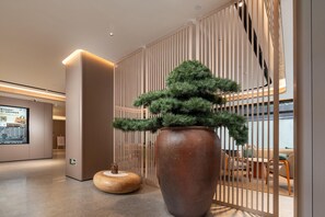 A modern interior with a large potted tree, a wooden stool, and a seating area with a view. - Ji Hotel (Guangzhou)