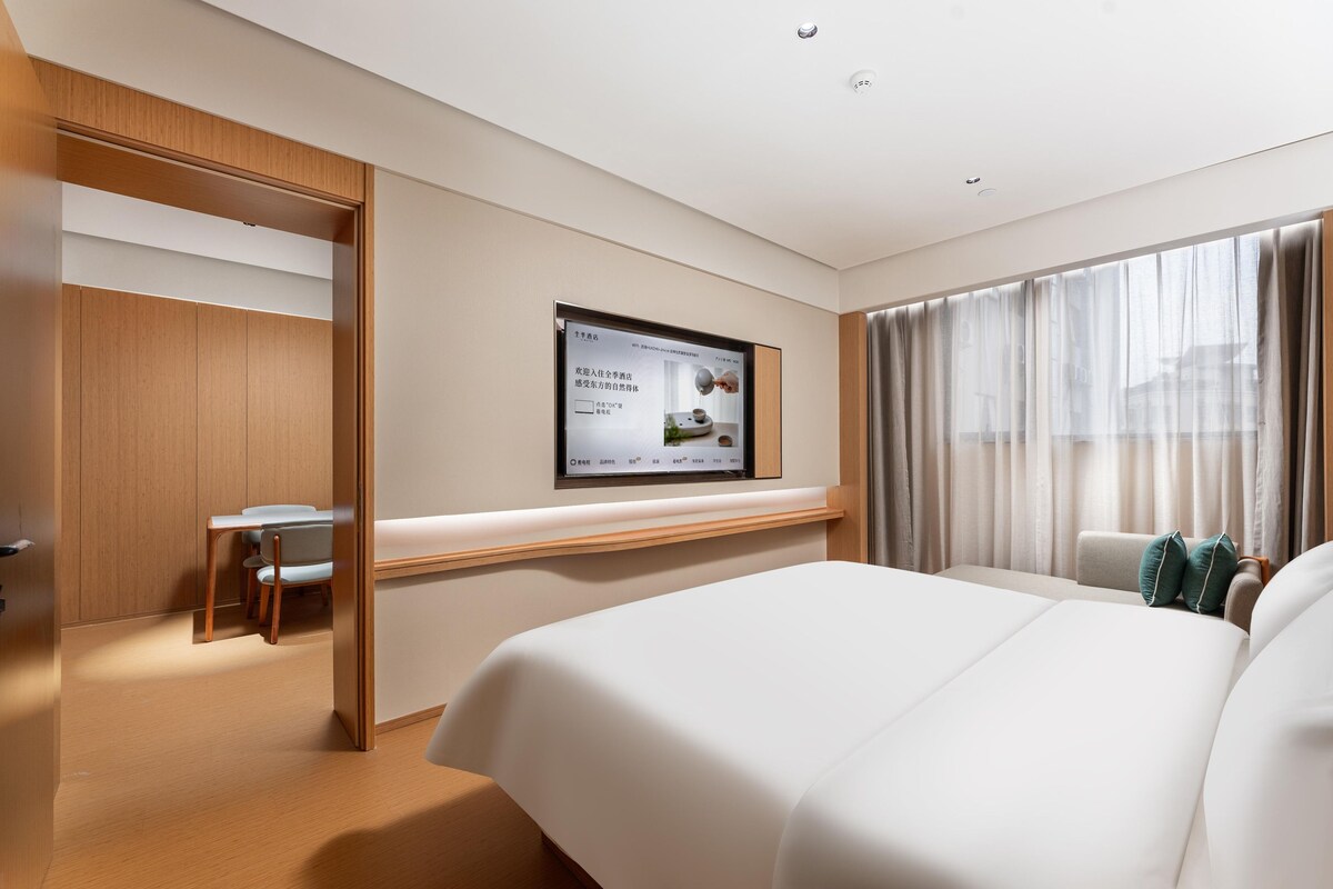 A hotel room with a bed, a desk, and a television mounted on the wall.