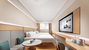 A hotel room with a bed, a seating area with a table, a TV mounted on the wall, and a window with curtains. - Ji Hotel (Guangzhou)