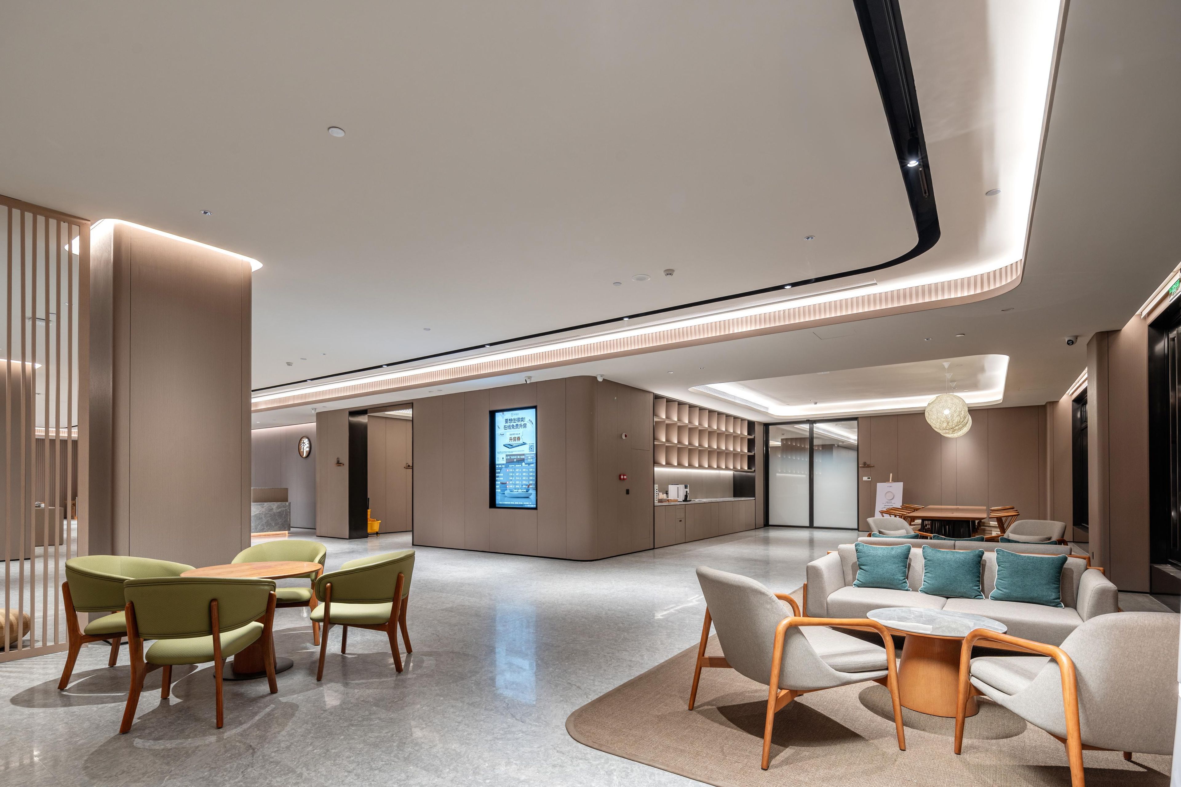 A modern hotel lobby with a reception desk, seating area, and a large digital display.