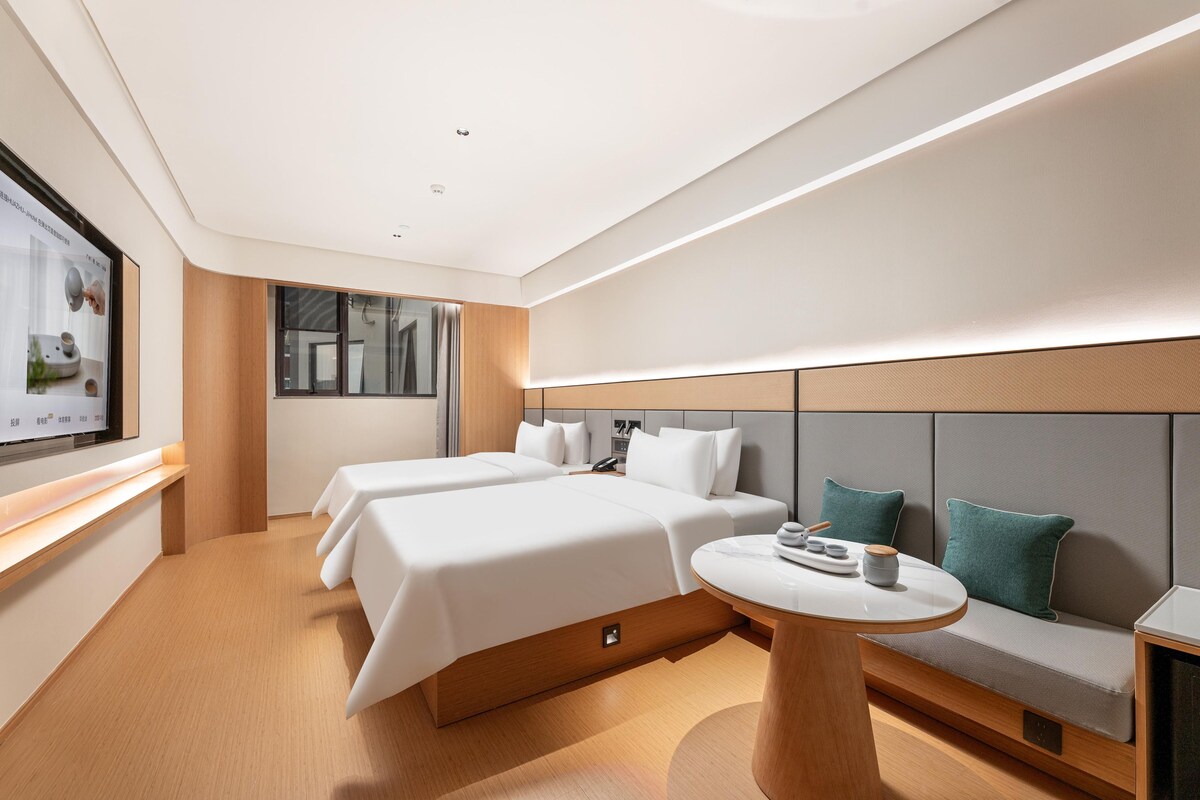 A modern hotel room with two beds, a small round table, and a seating area.