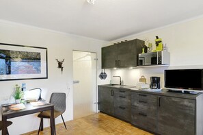 Moderni keittiö, jossa on ruokailutila, mikroaaltouuni, kahvinkeitin ja taulutelevisio.