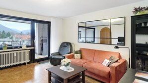 Een woonkamer met een bank, een salontafel, een stoel, een radiator, een raam en een boekenkast.