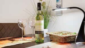 Een tafel met een fles Weissburgunder wijn, twee glazen, een rieten mand met eten en een lamp.